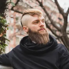 Mężczyzna z gęstą brodą i podgolonymi bokami głowy w czarnej bluzie.