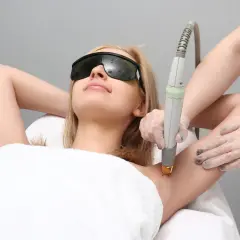 Kobieta w okularach ochronnych poddaje się depilacji laserowej pach. Czy depilacja laserowa boli? To zależy od indywidualnego progu bólu.