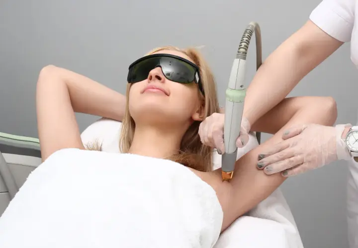 Kobieta w okularach ochronnych poddaje się depilacji laserowej pach. Czy depilacja laserowa boli? To zależy od indywidualnego progu bólu.