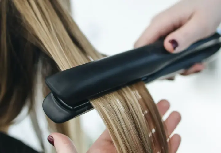 Dłoń trzyma prostownicę, wygładzając blond włosy. Nie wiadomo, ile stopni ma prostownica, ale efekt jest widoczny.