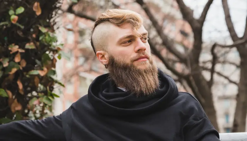 Mężczyzna z gęstą brodą i podgolonymi bokami głowy w czarnej bluzie.
