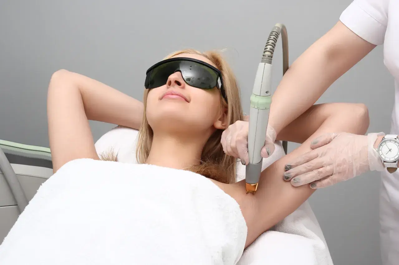 Kobieta w okularach ochronnych poddaje się depilacji laserowej pach. Czy depilacja laserowa boli? To zależy od indywidualnego progu bólu.